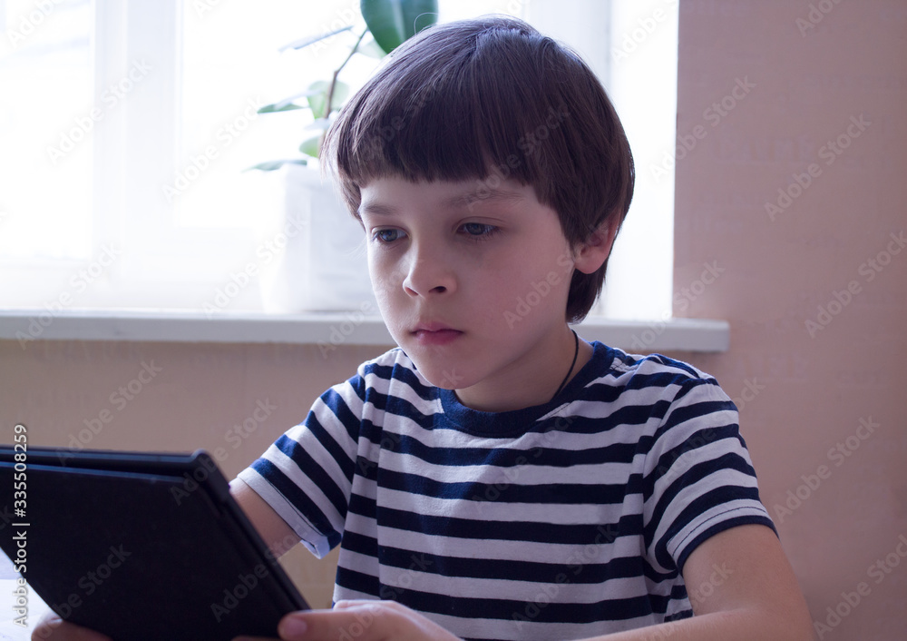 Distance learning. Online education.Schoolboy in a medical mask at home is doing homework on a laptop. School books and notebooks on the table Distance learning. Online education.Schoolboy in a medical mask at home is doing homework on a laptop. School books and notebooks on the table