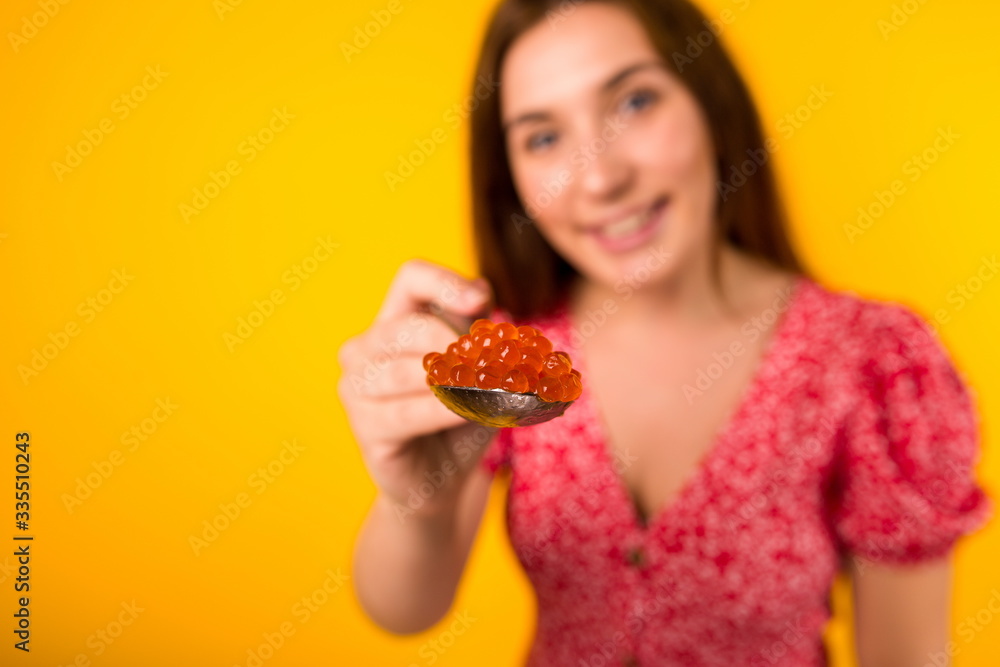 Beautiful girl on a yellow background holding out a spoon with red caviar forward. Posh life Beautiful girl on a yellow background holding out a spoon with red caviar forward. Posh life