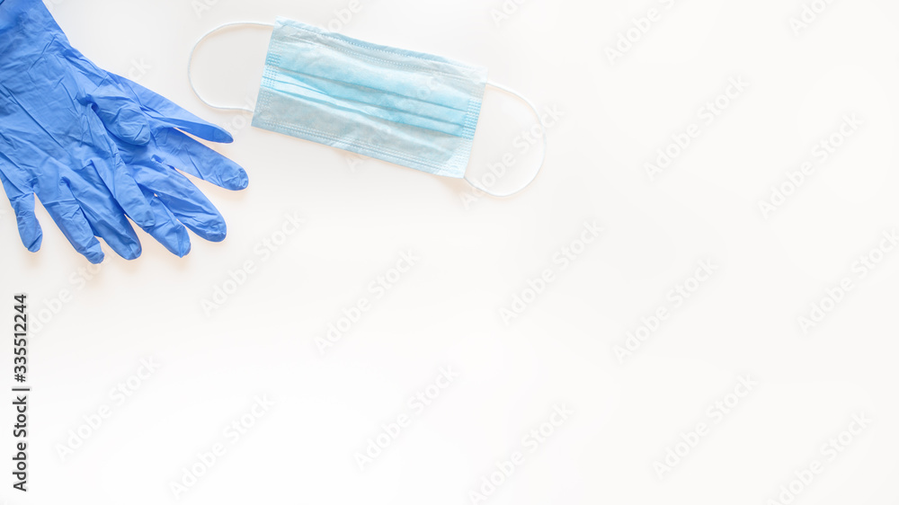 A pair of blue latex medical gloves lie on a white background next to a blue medical face mask: banner, text space, medical concept A pair of blue latex medical gloves lie on a white background next to a blue medical face mask: banner, text space, medical concept