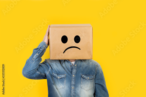 Hombre con caja de cartón en la cabeza con gesto pensativo y mano en la cabeza sobre fondo amarillo liso brillante aislado. Vista de frente y de cerca. Copy space