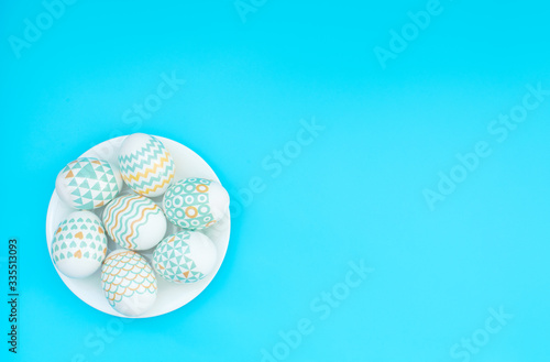 Decorated Easter eggs lie on the white plate on blue background. Happy Easter holiday concept. Greeting, invitation card. Flat lay style with copy space.