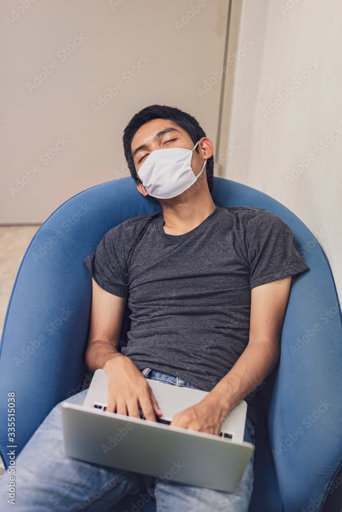Covid-19, Man wearing face mask sleeping on sofa with laptop computer, Wearing a face mask to protect against coronavirus, business report. Work from home.