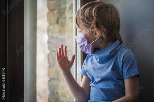 a little boy looks out the window in a medical mask © tankist208