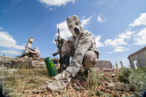 Two soldiers in the gas masks and protective clothes are testing biological weapon on the ruined background.