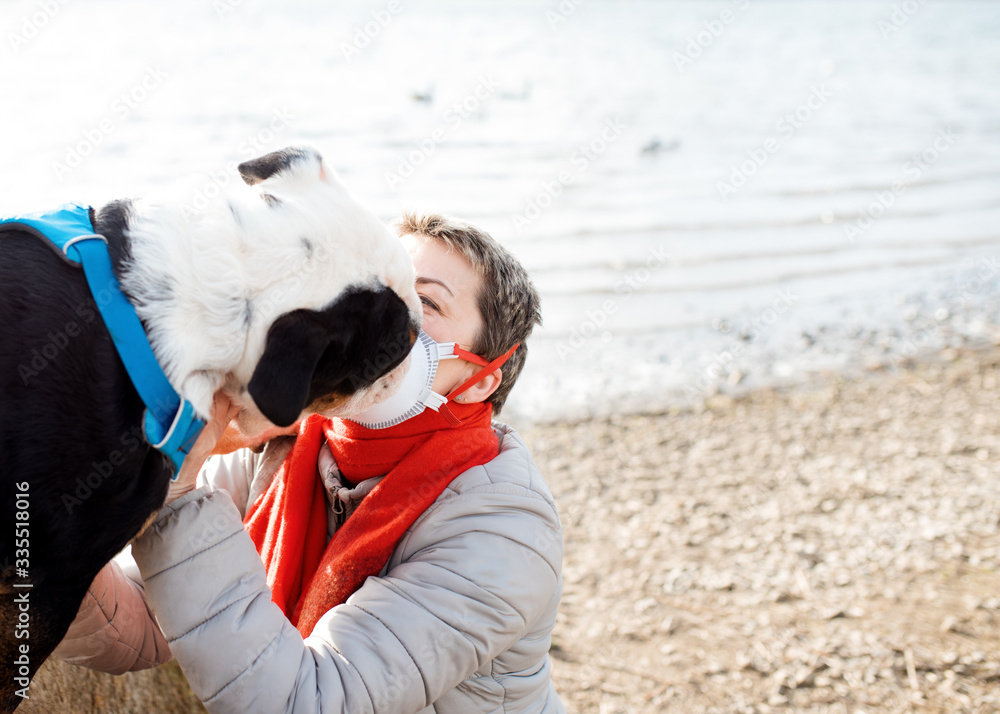 Woman wearing white and red a face mask, and red scarf, stroking and hugging a dog outdoors Woman wearing white and red a face mask, and red scarf, stroking and hugging a dog outdoors