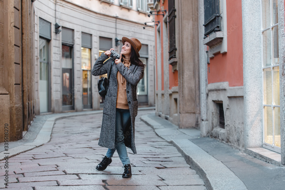 A young girl tourist in a fashionable brown hat is walking along a narrow street and taking pictures. Amid beautiful old buildings. A young girl tourist in a fashionable brown hat is walking along a narrow street and taking pictures. Amid beautiful old buildings.