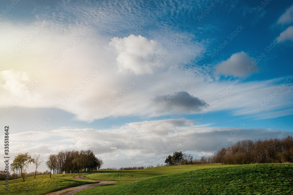 Green grass golf fields, a few trees, dramatic cloudy blue sky  in South Yorkshire in the warm sunny spring day