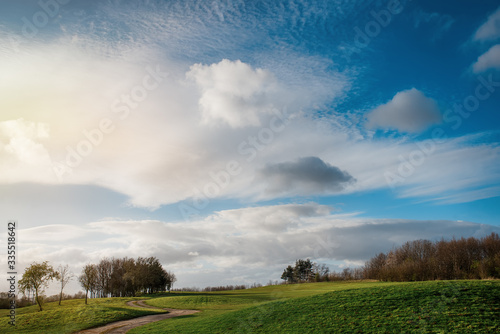 Green grass golf fields  a few trees  dramatic cloudy blue sky  in South Yorkshire in the warm sunny spring day
