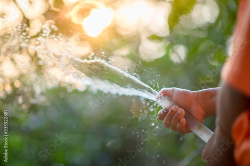 The little boy's hand is played with a hose in a sunny backyard. Preschoolers are fun with water spray. Off-Summer Activities for Children