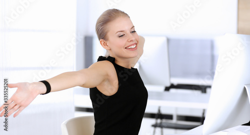 Business woman happy and excited while working with computer in modern office. Secretary or female lawyer looks beautiful in black dress. Raised arms because of emotion. Business people concept