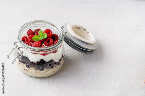 Overnight oatmeal with raspberries, blueberries, and yogurt in a jar isolated on grey background. Healthy vegetarian breakfast. Copy space. 