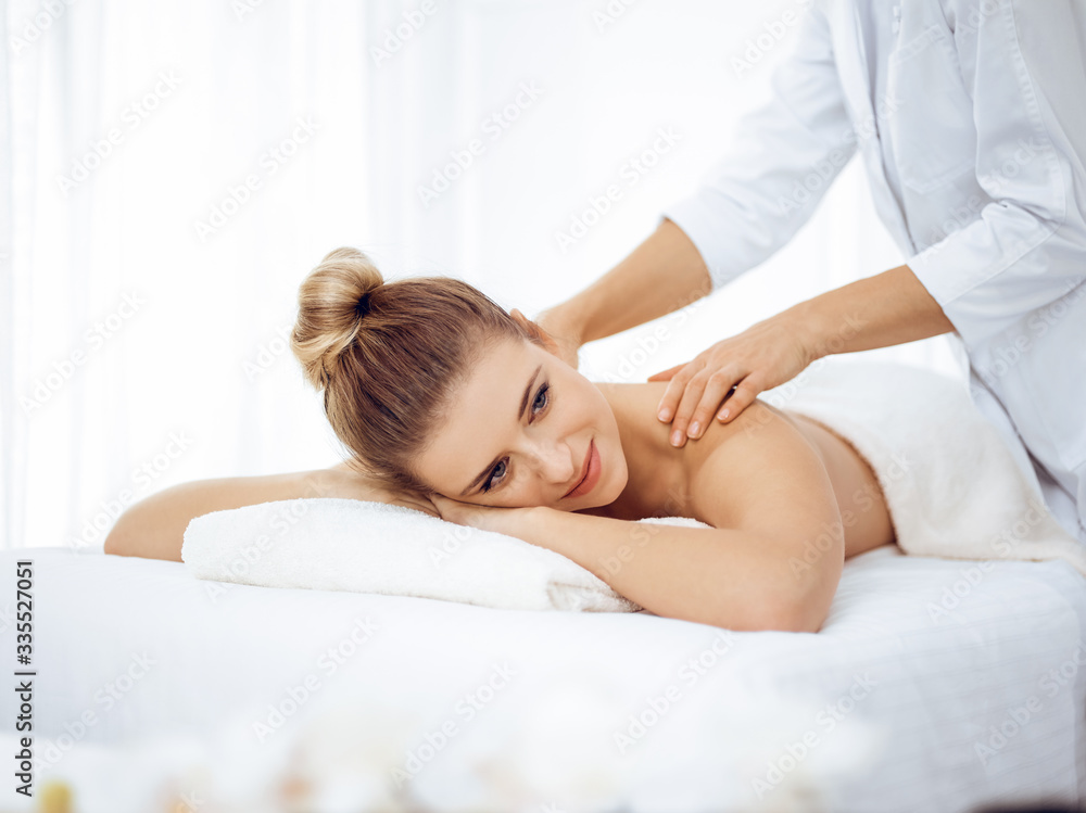 Young and blonde woman enjoying massage of back in spa salon. Beauty concept Young and blonde woman enjoying massage of back in spa salon. Beauty concept