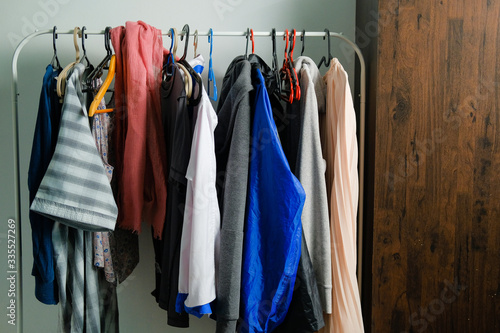 Collection of colorful clothes and jacket for male and female hanging on a rack by the window at home.