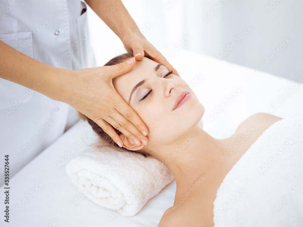 Young and blonde woman enjoying facial massage in spa salon. Beauty concept Young and blonde woman enjoying facial massage in spa salon. Beauty concept