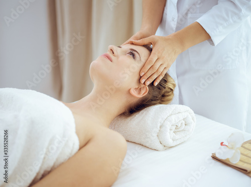 Young and blonde woman enjoying facial massage in spa salon. Beauty concept