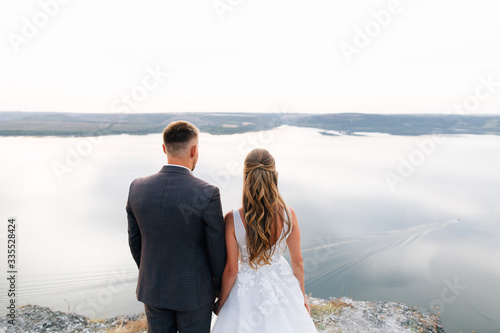 Groom and bride holding each others hands and looking at sunset. Outdoor engagement concept.