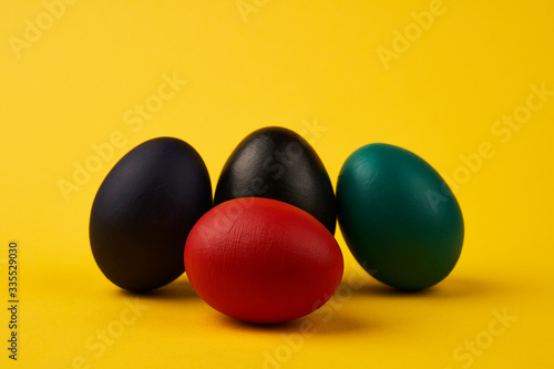 Colored black green blue red easter eggs on bright yellow background