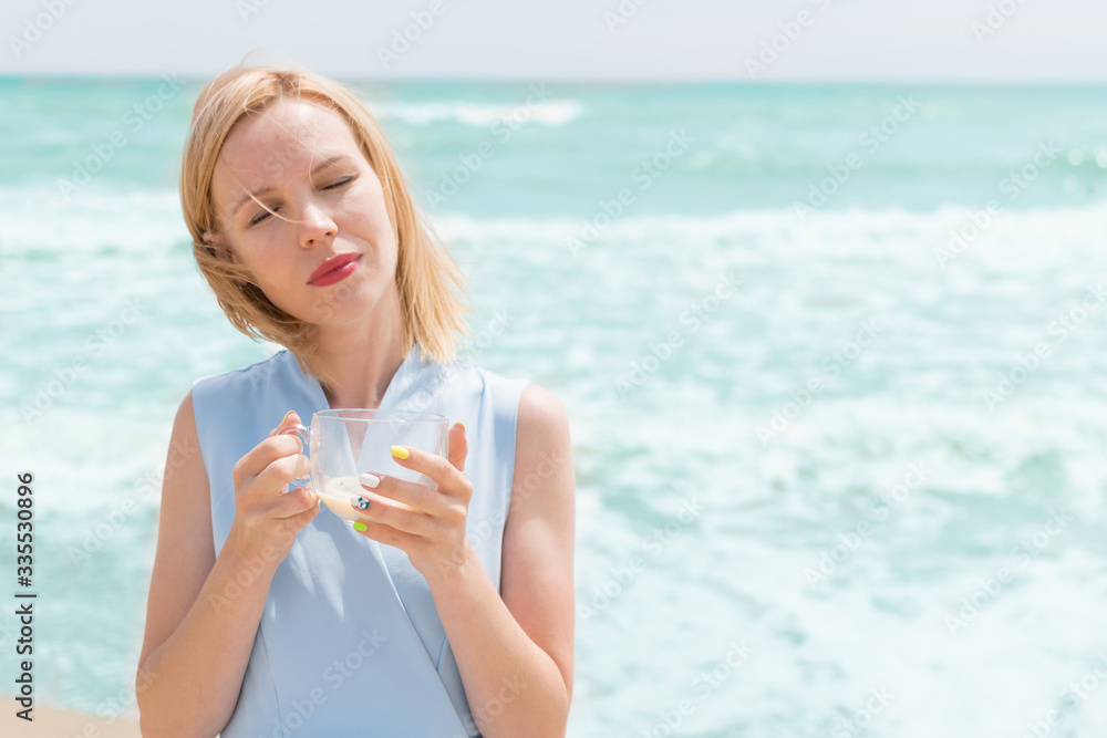 A woman is drinking tea with milk from a large cup on the ocean, the sea. A woman is drinking tea with milk from a large cup on the ocean, the sea.