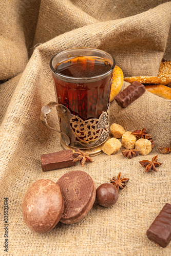 A faceted glass of tea in a vintage Cup holder, bagels, cookies, chocolate gingerbread and star anise on a background of rough-textured fabric. Close up.