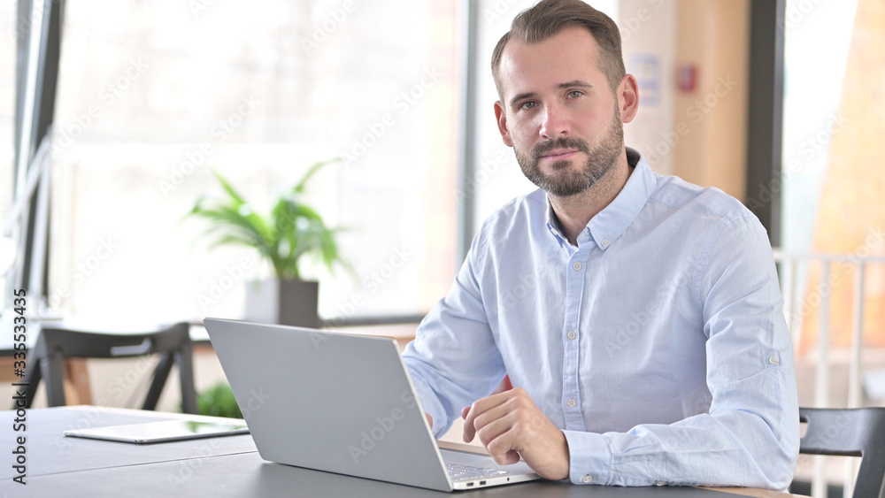 Fototapeta premium Young Man with Laptop Looking at Camera in Office