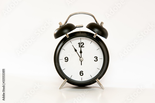 Vintage alarm clock with simple and minimalist design, isolated on white background. 5 to 12 o'clock at noon / midnight.