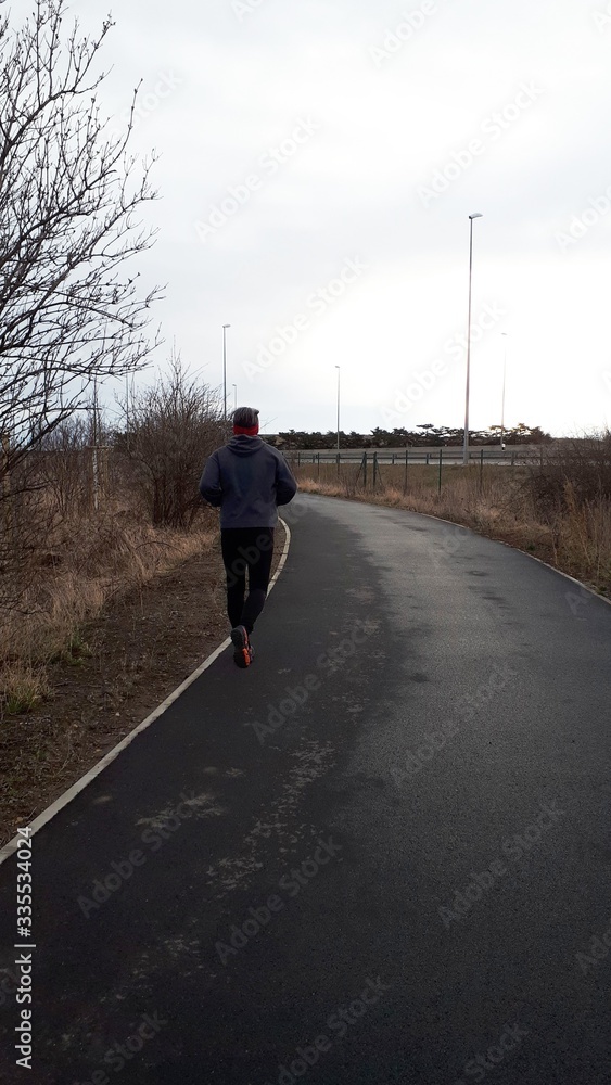A man is Jogging on the park. Sport is a healthy lifestyle. The boy runs on an asphalt path in a park. Rear view of a running man. Copy space for your text.