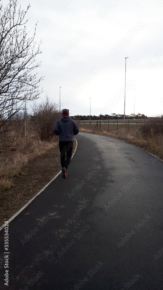 A man is Jogging on the park. Sport is a healthy lifestyle. The boy runs on an asphalt path in a park. Rear view of a running man. Copy space for your text. A man is Jogging on the park. Sport is a healthy lifestyle. The boy runs on an asphalt path in a park. Rear view of a running man. Copy space for your text.