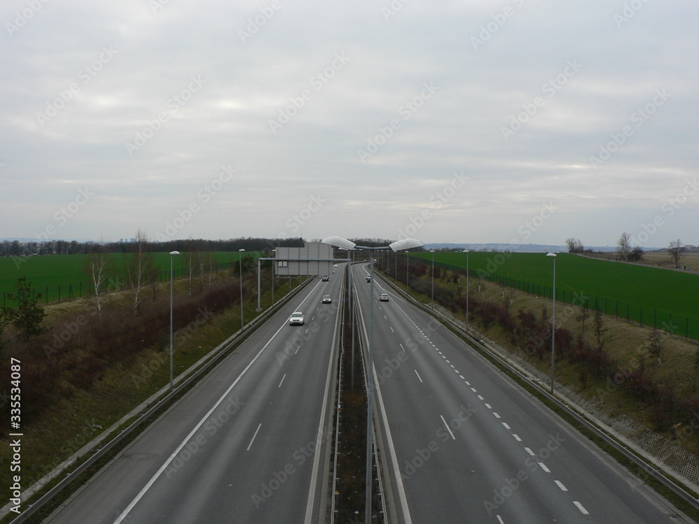 Empty highway on a cloudy day. A speeding car. View over the two-way road with two lanes in each direction. 