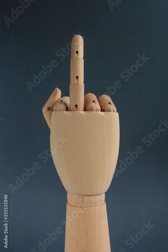 A wooden hand showing the middle finger, an offensive vulgar gesture on a gray background. photo