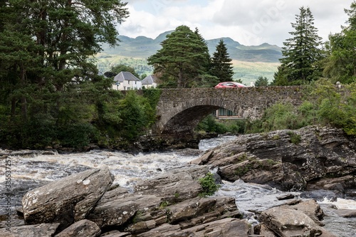 The historical stone bridge of the A827 road above the river and falls of Dochart in Killin, Scotland with a red car with motion blur effect