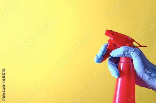 The girl holds in hands a red spray bottle on a yellow background