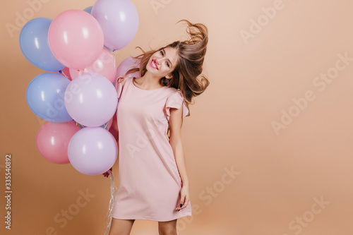Wonderful long-haired woman funny dancing with colorful helium balloons. Studio shot of ecstatic birthday girl expressing happiness.