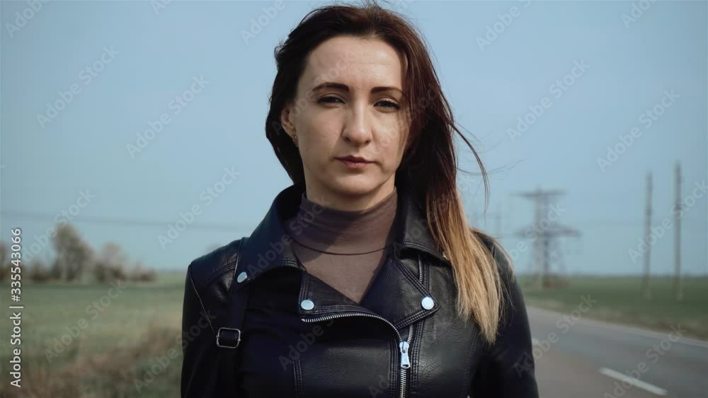 Close up caucasian young woman tourist looking into camera while walking outdoors on road with white car. Female hitchhiking around country Close up caucasian young woman tourist looking into camera while walking outdoors on road with white car. Female hitchhiking around country