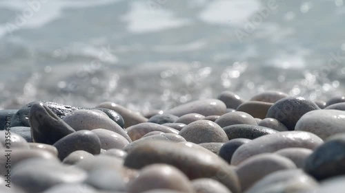 Close up to rocky beach pebbles on shore and rolling turquoise sea waves splashing photo