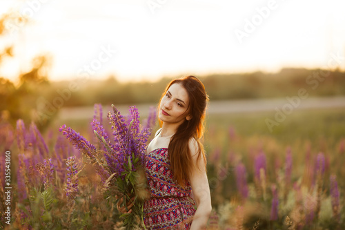 Young girl stand in field overlooking lavender field. Smiling carefree caucasian girl in dress enjoying the sunset