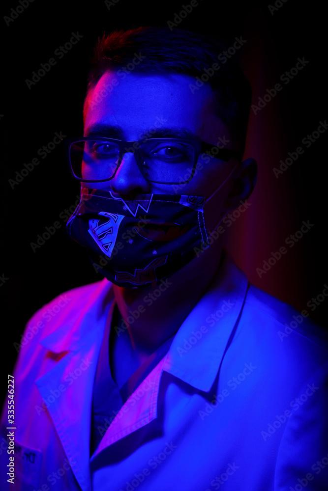 Doctor wears mask. Black background with blue - red light. Doctor in glasses closed mouth with medical mask. Close up shot Doctor wears mask. Black background with blue - red light. Doctor in glasses closed mouth with medical mask. Close up shot
