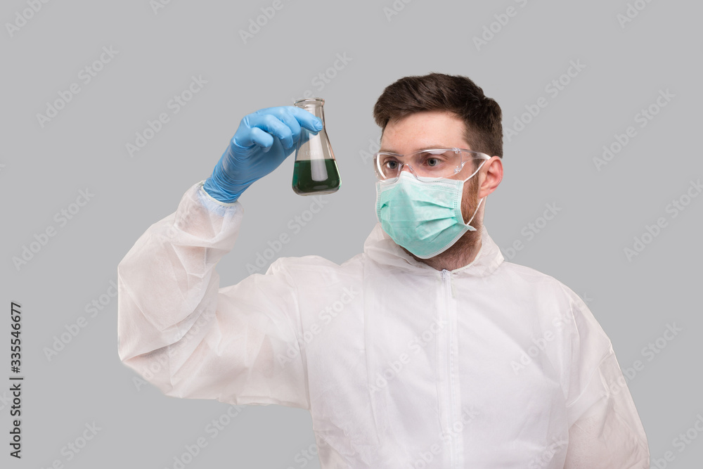 Male Laboratory Worker in Chemical Suit, Wearing Medical Mask and Glasses Watching Flask with Colorfull Liquid. Science, Medical, Virus Concept Male Laboratory Worker in Chemical Suit, Wearing Medical Mask and Glasses Watching Flask with Colorfull Liquid. Science, Medical, Virus Concept