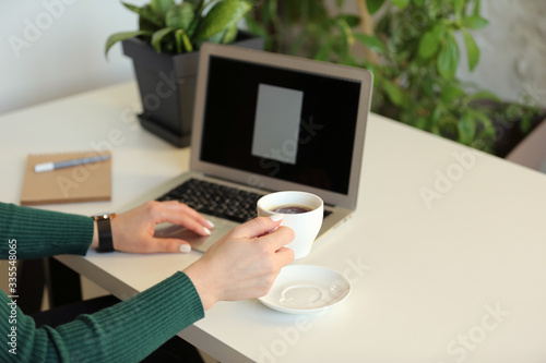 Office employee sits at a table, works at a laptop and drinks coffee