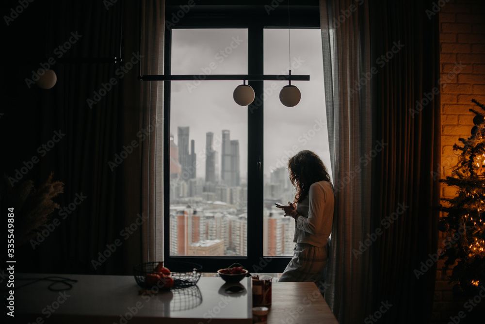 young woman in pyjamas texting on her phone by the window young woman in pyjamas texting on her phone by the window