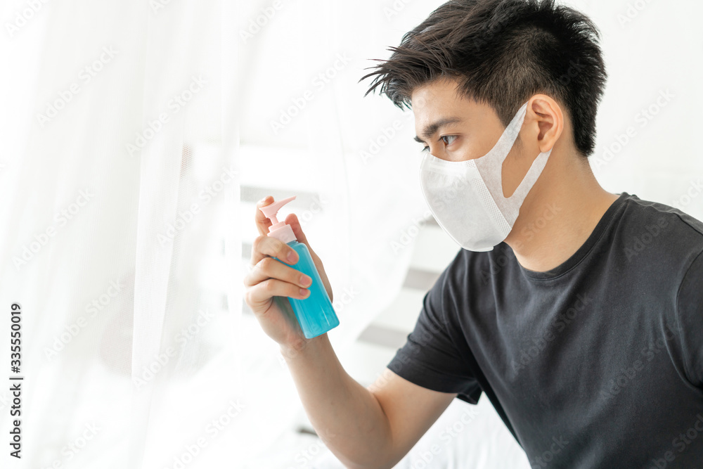 Asian man wearing Face Mask holding Alcohol for washing hands to protect Coronavirus covid-19 in quarantine room , Quarantine yourself to protect spread Covid-19