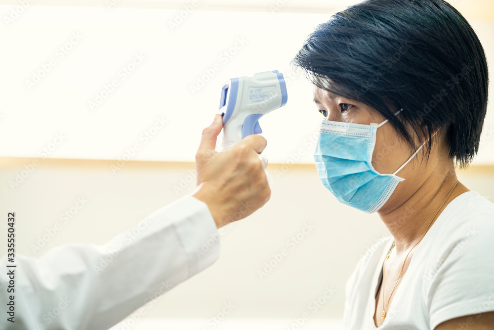 Female doctor check Asian woman body temperature using infrared forehead thermometer (thermometer gun) for virus symptom at hospital. Corona virus, Covid-19, quarantine or virus outbreak concept Female doctor check Asian woman body temperature using infrared forehead thermometer (thermometer gun) for virus symptom at hospital. Corona virus, Covid-19, quarantine or virus outbreak concept