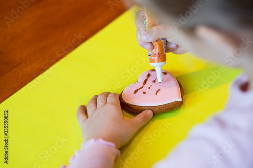 Child decorats gingerbread cookies for mom. Homemade bakery. Kids decorating freshly baked gingerbread cookies with icing and confectionery mastic. Festive food, family culinary. Master class photo