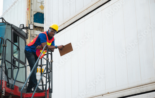 Black foreman worker working control the crane and forklift at Container cargo harbor to loading containers. African dock male staff for Logistics import export shipping concept.