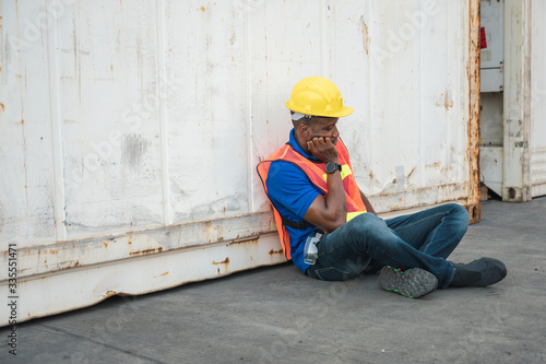 Tired depressed black foreman worker working at Container cargo harbor to loading containers. African dock male staff fall asleep for Logistics import export shipping concept.