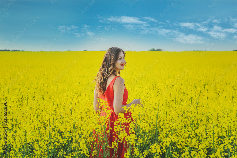 Young beautiful girl in a red dress close up in the middle of the yellow field with the radish flowers closeup Young beautiful girl in a red dress close up in the middle of the yellow field with the radish flowers closeup