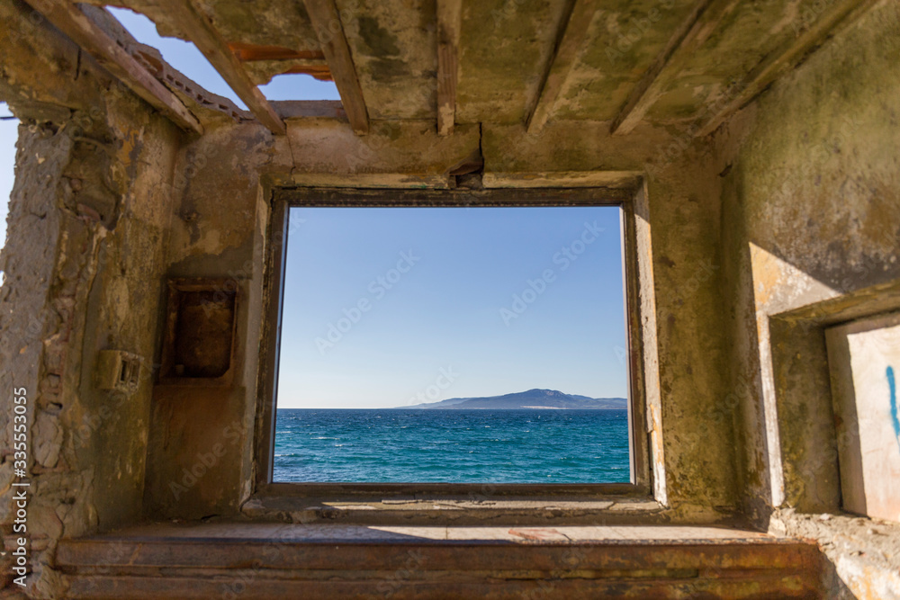 from a window we observe the outside landscape, we can see the calm blue sea on a clear day