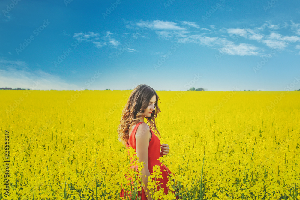 Young beautiful girl in a red dress close up in the middle of the yellow field with the radish flowers closeup Young beautiful girl in a red dress close up in the middle of the yellow field with the radish flowers closeup