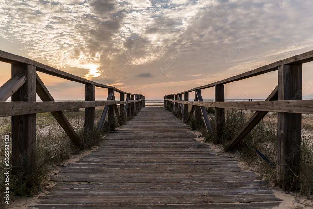 wooden walkway of the beach from which we see the sunset on a day with clouds