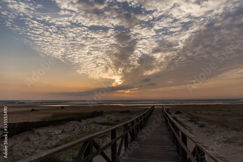 wooden walkway of the beach from which we see the sunset on a day with clouds © Eloy