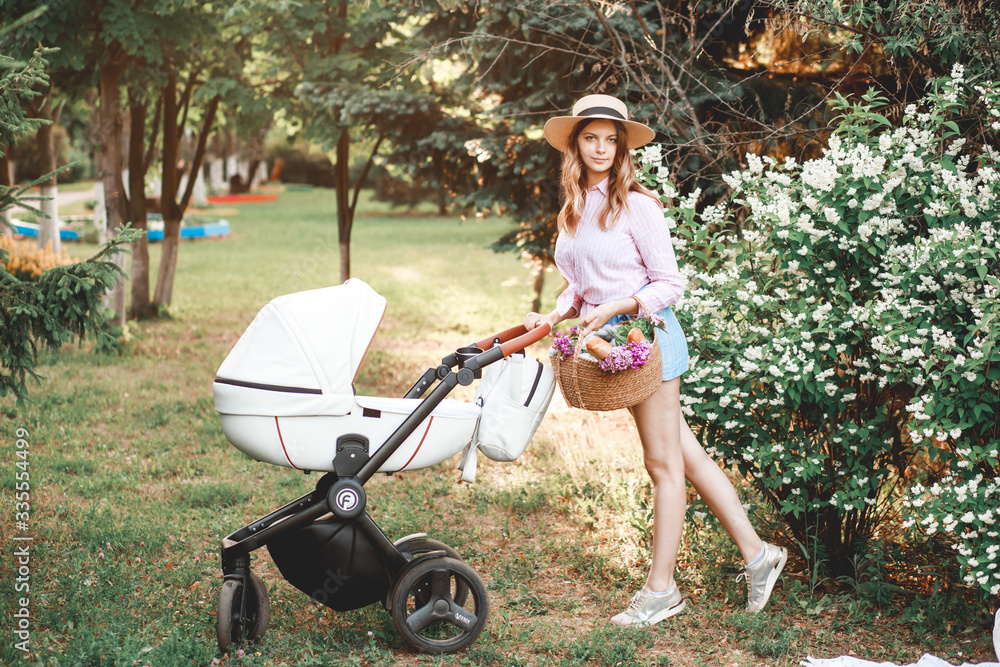A woman is walking with a baby stroller on the path in the park at sunset. A woman is walking with a baby stroller on the path in the park at sunset.